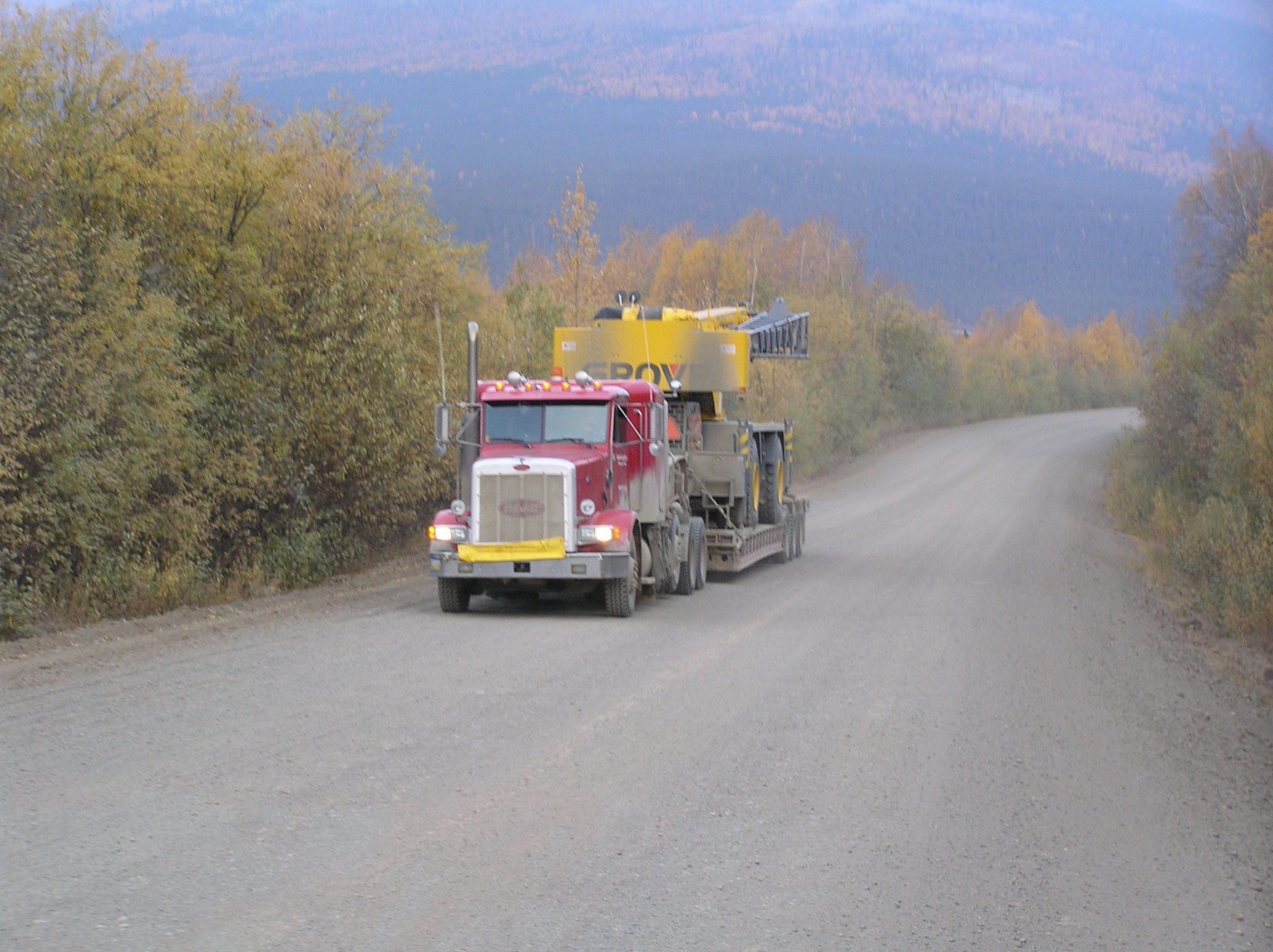 Red semi truck driving on a road in alaska. There is a montain in the background.